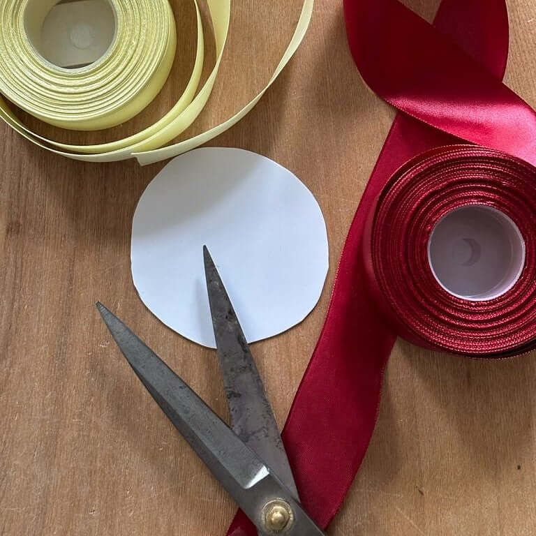 Rouleaux de ruban satin jaune pâle et rouge, cercle de papier découpé et vieux ciseaux sur une table en bois