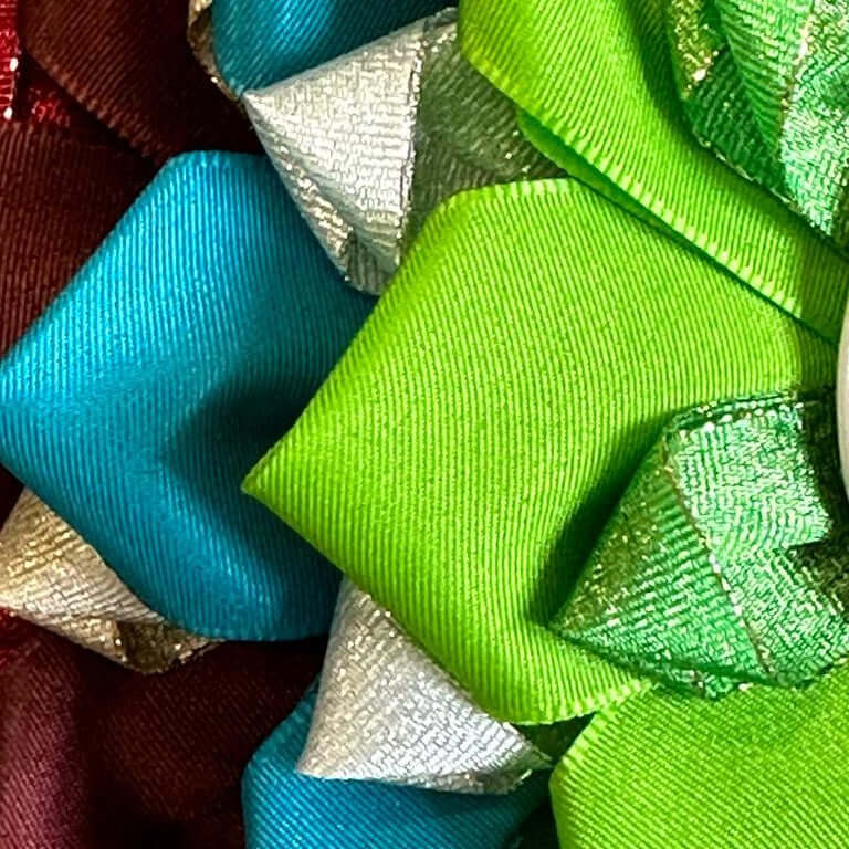 Gros plan sur les rubans plissés d’une cocarde en satin turquoise, vert citron, argent, vert métallisé et bordeaux