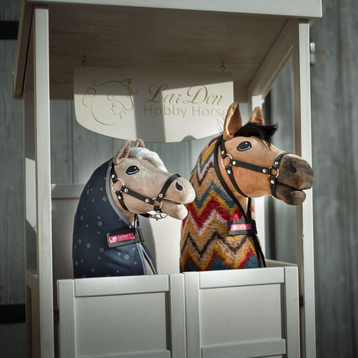 Twee Hobby Horses in een witte houten box met bord LarDen Hobby Horse, in een marineblauwe gestipte en een kleurrijke zigzagdeken