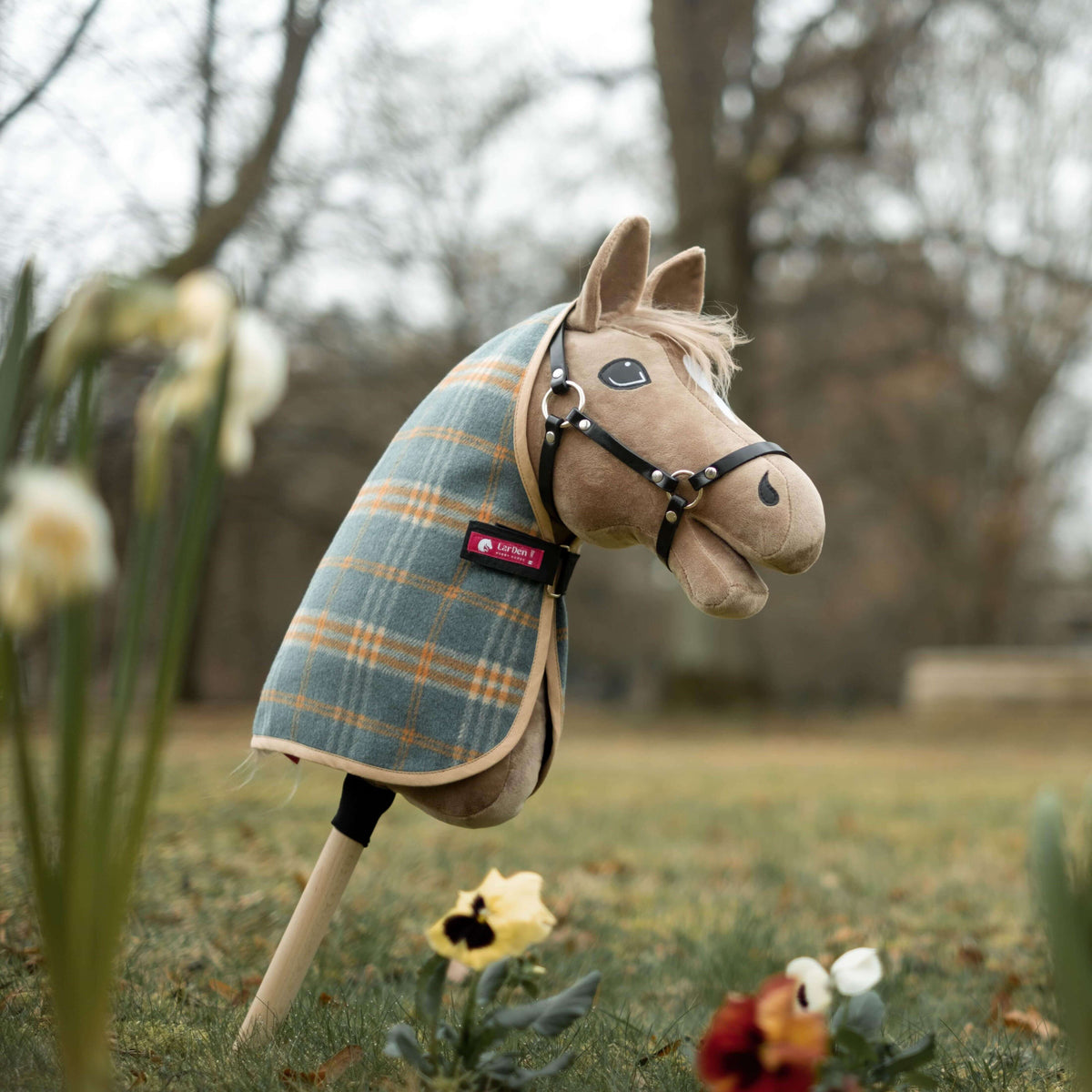 Lichtbruine Hobby Horse met zwarte halster in een petrol-oranje geruite staldeken met roze LarDen label