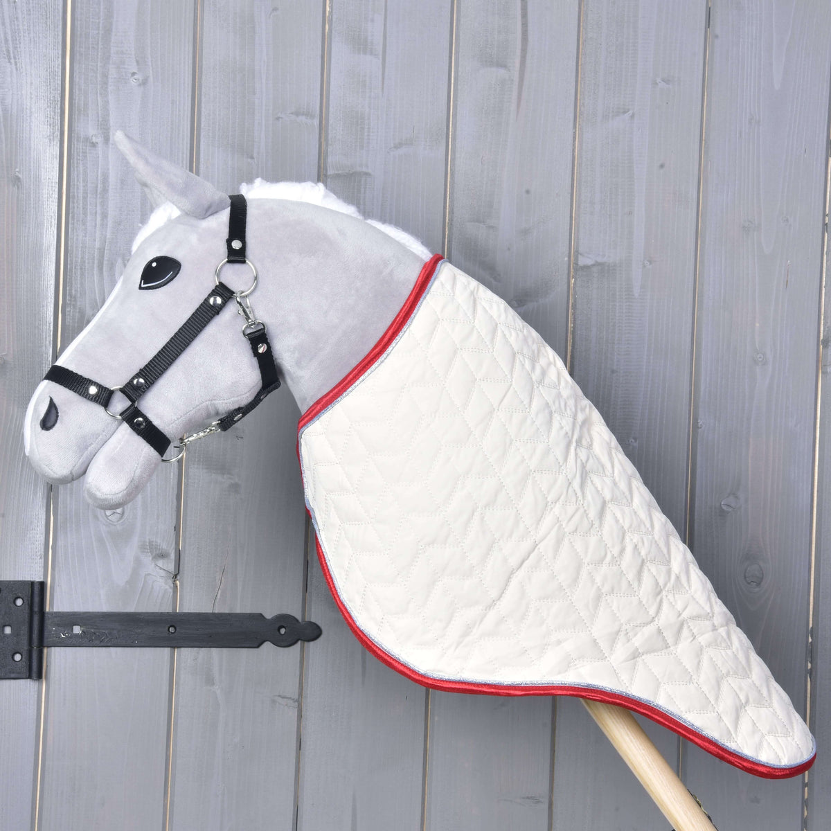 Grijze Hobby Horse in profiel met de crème gewatteerde reisdeken, die de hals tot aan de houten stok bedekt