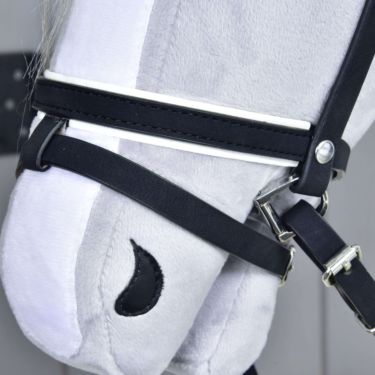 Close-up of the black noseband with white piping and the lower strap around the muzzle, with silver buckles and clips