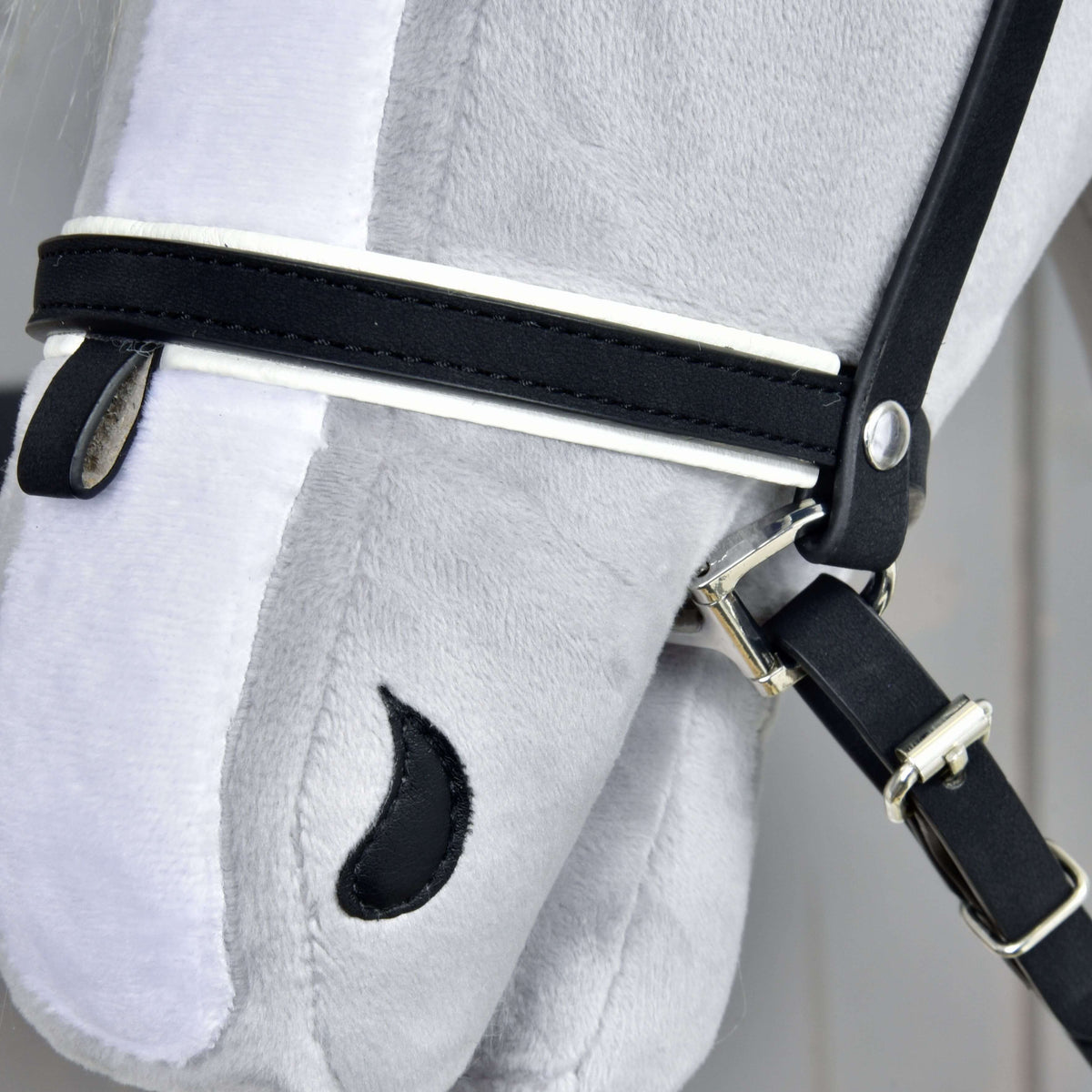 Close-up of the white-piped noseband with its keeper loop, silver rivet and buckle on the cheekpiece of the black bridle