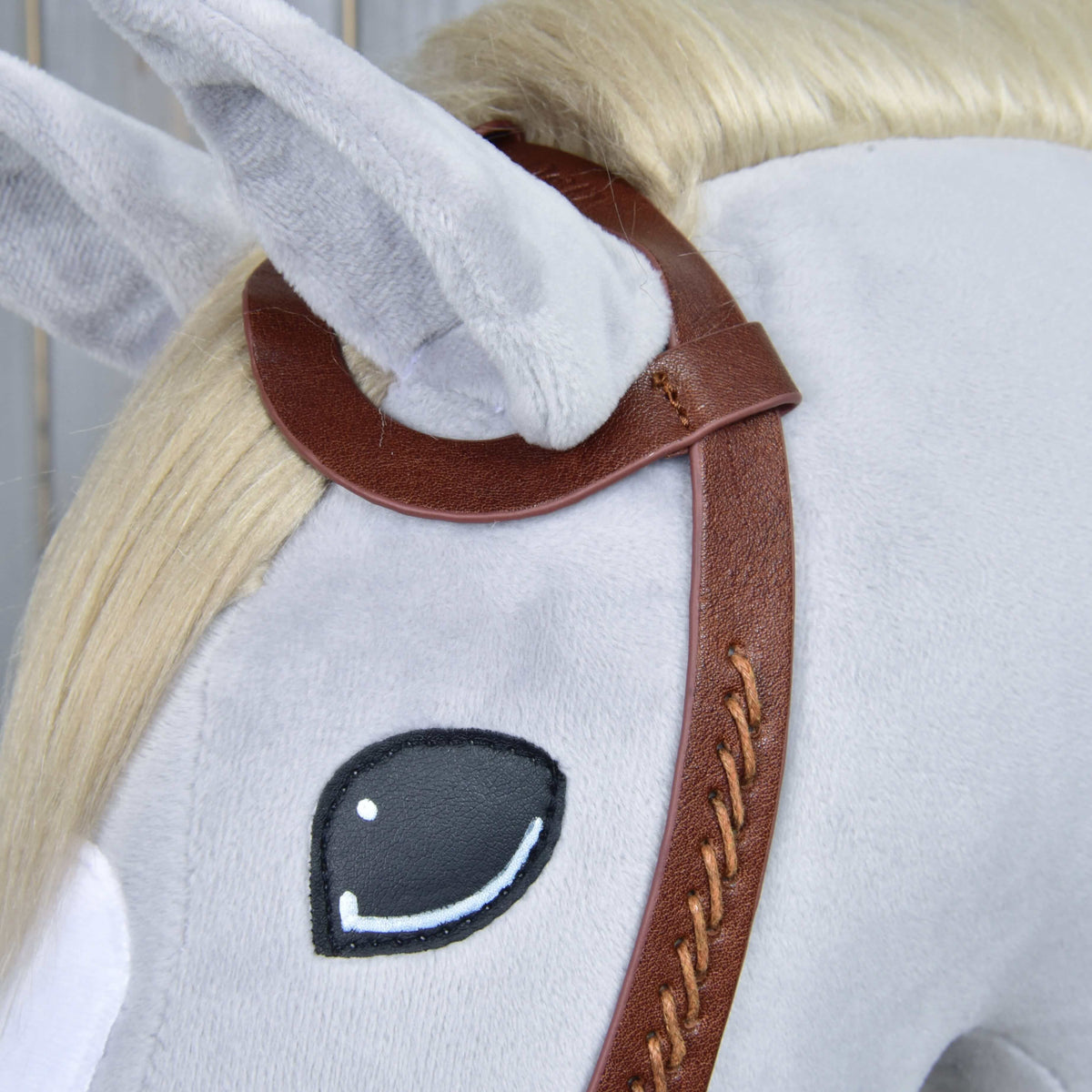 Close-up of the brown ear loop around one plush ear and the cheekpiece with tan cross-stitching beside the eye