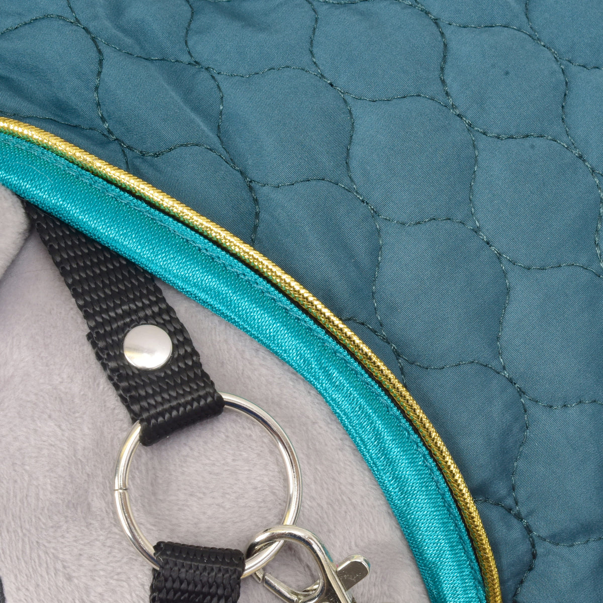 Close-up van de halsrand van de Lagoon met turquoise rand en gouden bies naast een zwart halsterbandje en zilveren ring