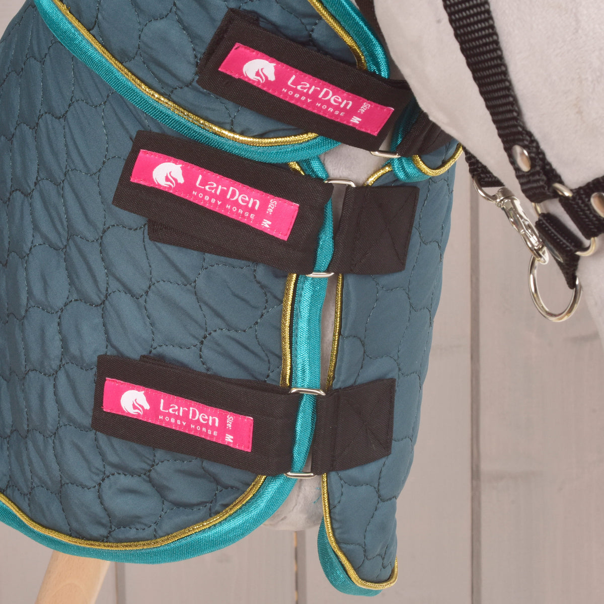 Drie zwarte borstriempjes met roze LarDen-labels gesloten op de deken Lagoon van een grijze Hobby Horse met zwart halster