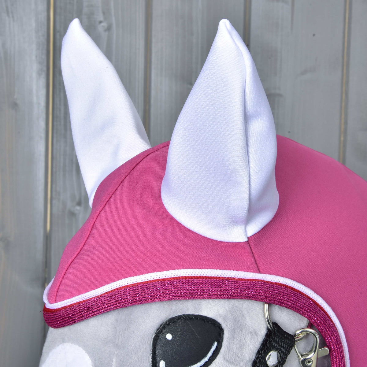 Close-up van de kap van de Regenjas LarDen op een grijze Hobby Horse: witte oren op frambozenroze met glinsterende roze rand