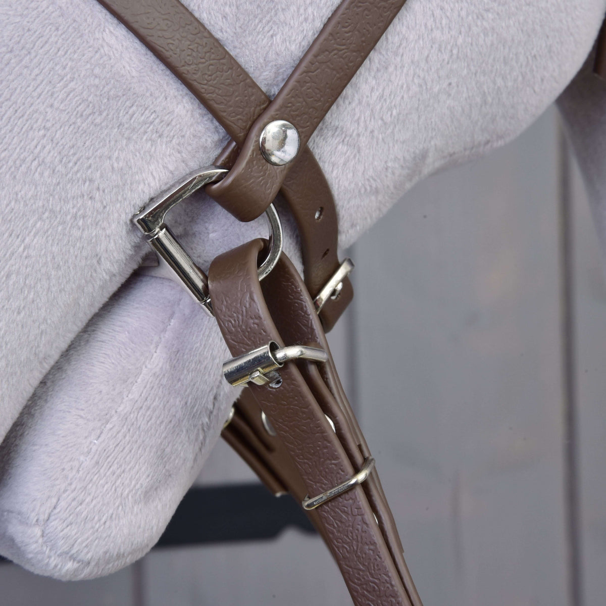Close-up of the brown leatherette noseband, bit ring and rein clip with silver buckles on a grey Hobby Horse
