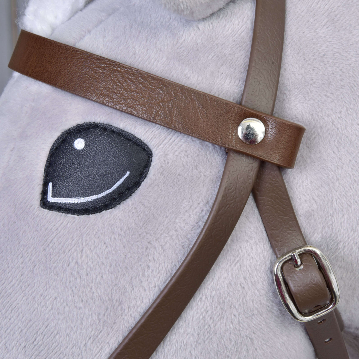 Close-up of the brown leatherette browband with silver rivet and cheek buckle beside the eye of a Hobby Horse