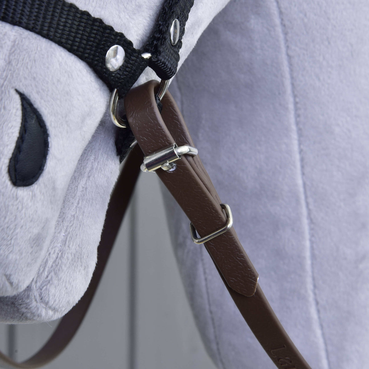Close-up of the brown rein buckle, keeper and loop fastened to the halter ring under the chin of a grey Hobby Horse
