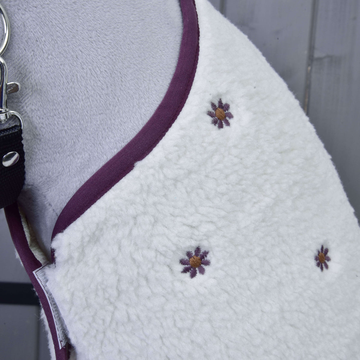 Detail van de kleine geborduurde pruimkleurige bloemetjes met goudkleurig hart op de crèmekleurige teddydeken bij de hals