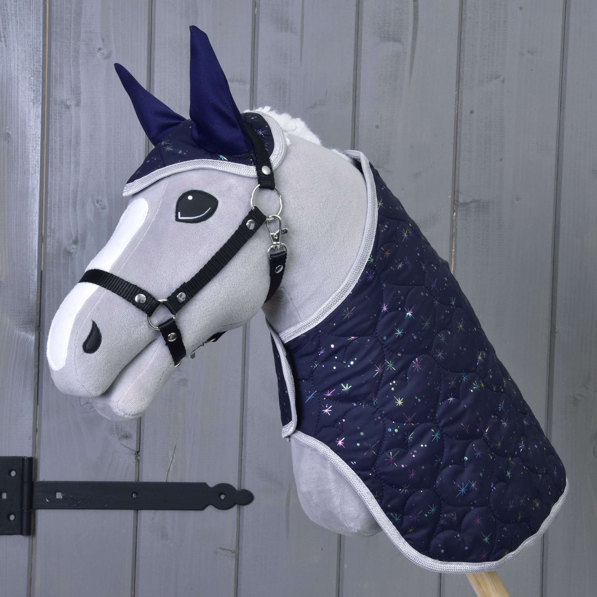 Grijze pluche Hobby Horse met zwart halster draagt de marineblauwe deken en het oornetje van Set Magic met glinsterende sterren