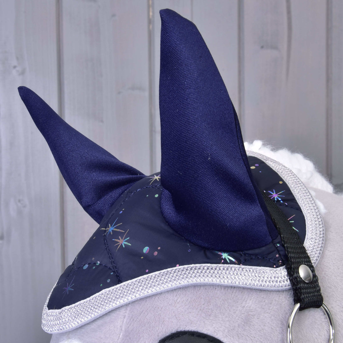 Close-up van het oornetje uit Set Magic met hoge marineblauwe oren, holografische sterrenprint en gevlochten grijze rand