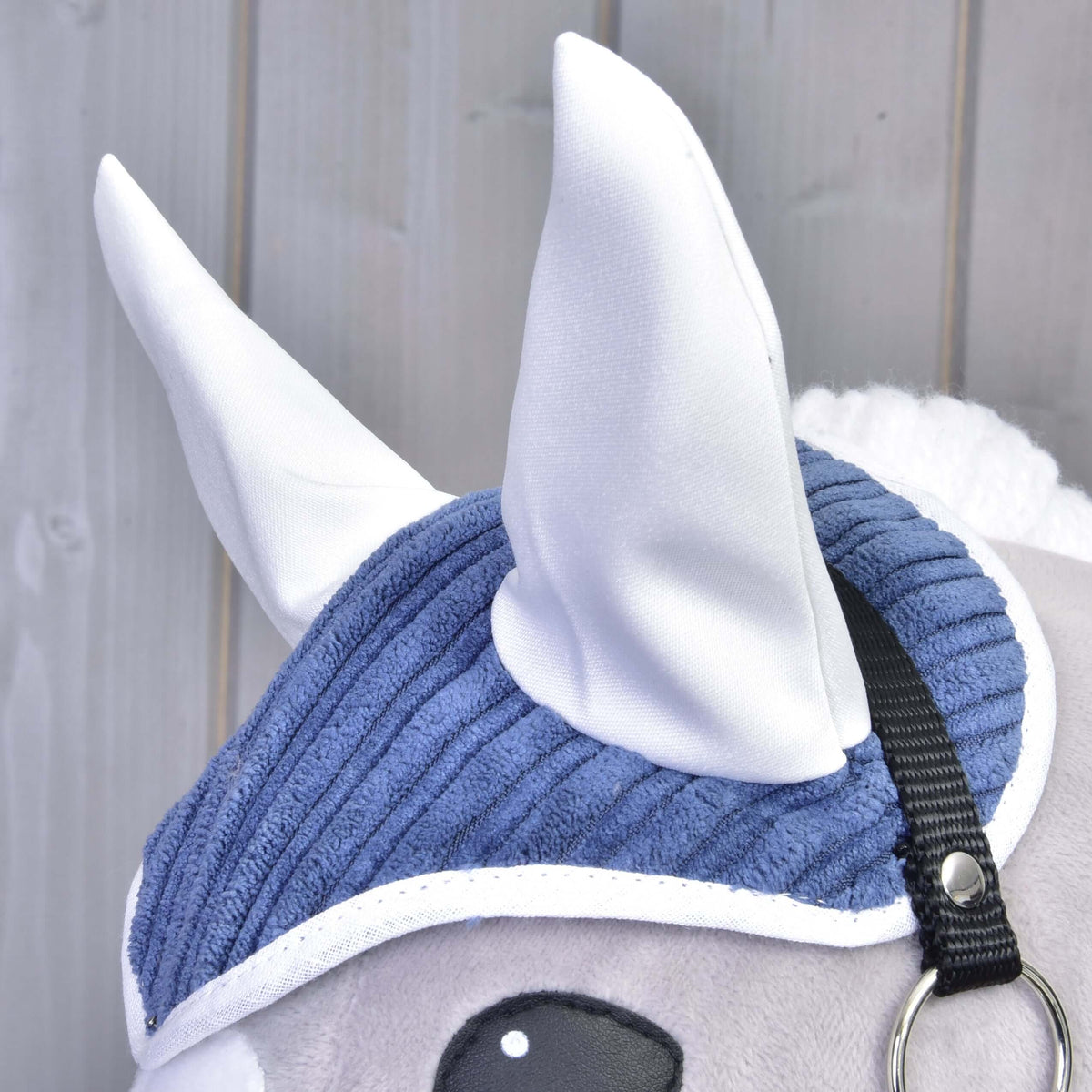 Gros plan sur le bonnet d’oreilles de l’ensemble Manchester Plum en velours côtelé bleu, oreilles et liseré blancs, sur un Hobby Horse gris