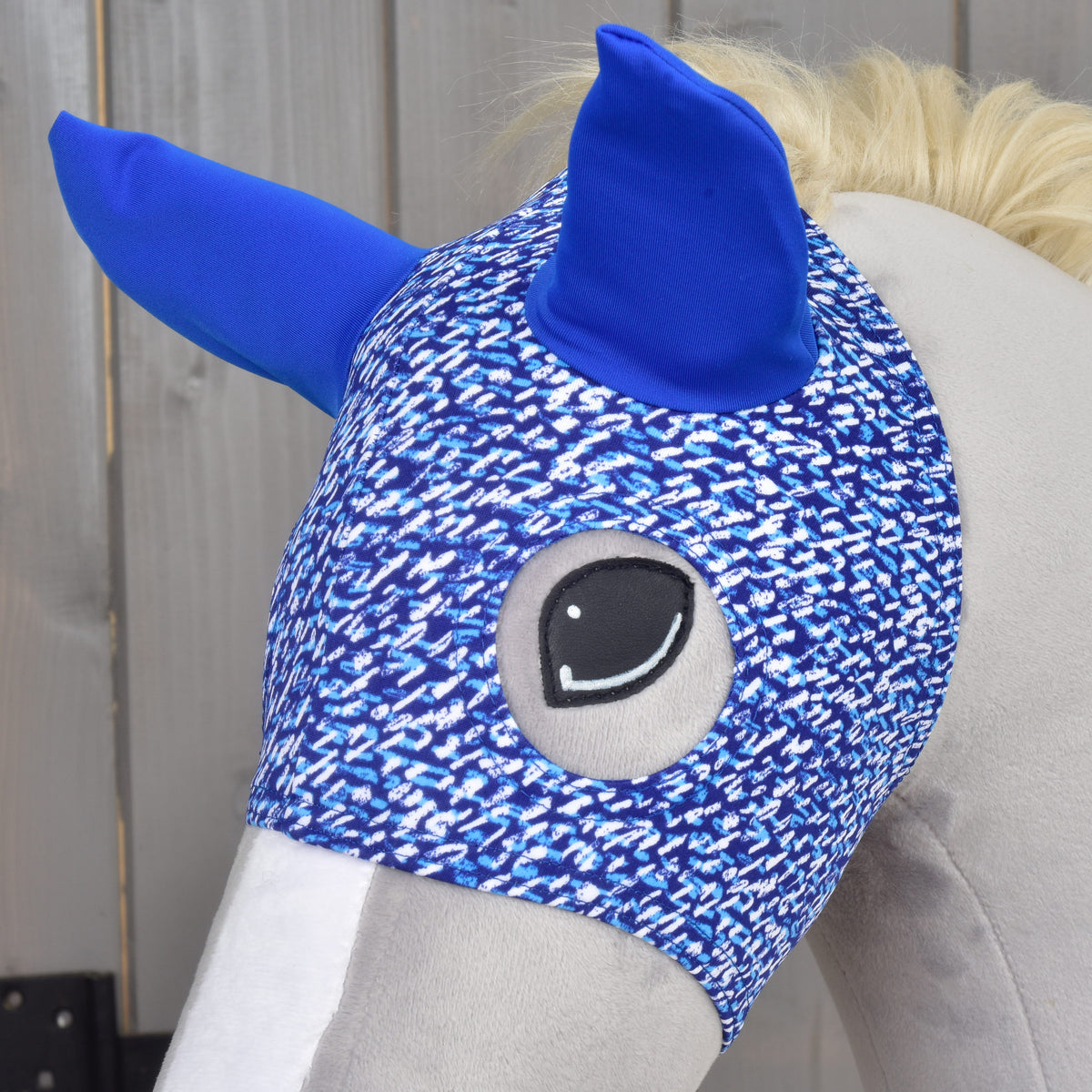 Close-up van het paardenmasker See op een grijze Hobby Horse, het geborduurde oog omlijst door de blauw gespikkelde stof