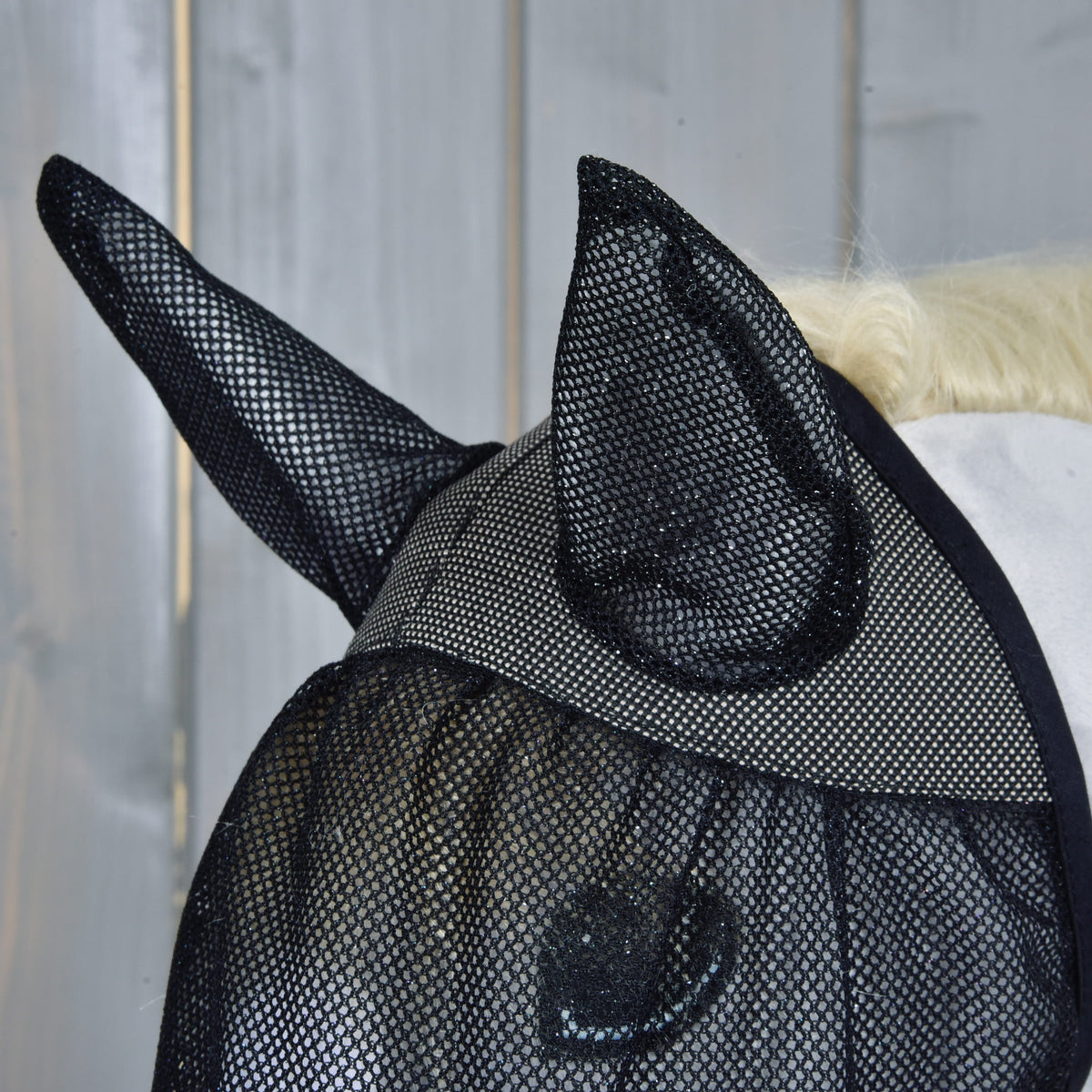 Vliegenmasker van opzij met rechtopstaande gazen oren en fijn zwart gaas over het oog van een lichtgrijze Hobby Horse