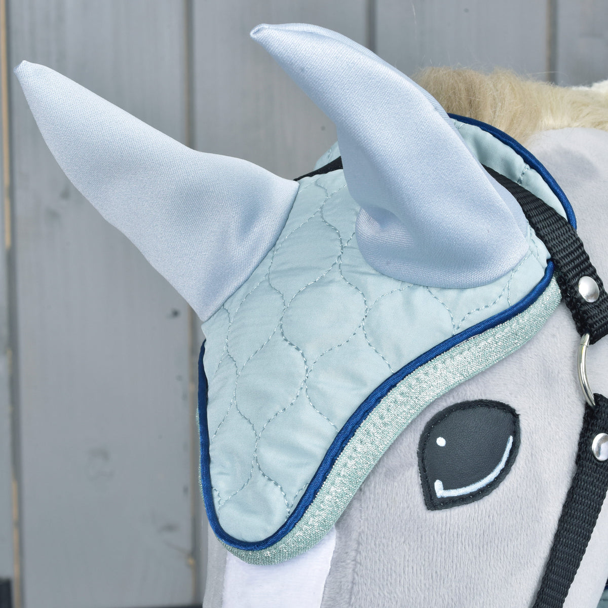 Gros plan sur le bonnet d'oreilles de l'ensemble Mint sur un Hobby Horse gris : matelassage et oreilles bleu pâle, passepoil marine et paillettes