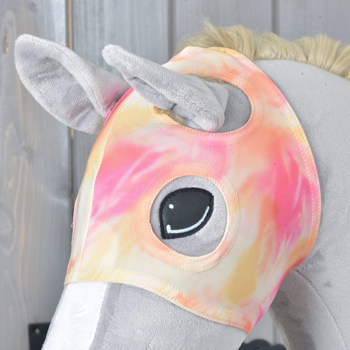 Close-up van het masker Mirage op een grijze Hobby Horse, de pluche oren steken erdoor en de oogopening is netjes gestikt