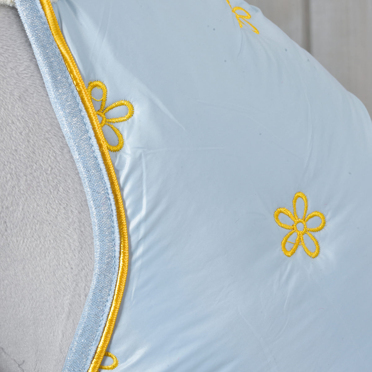 Gros plan sur les fleurs brodées jaunes et le passepoil jaune de la couverture d’écurie Hobby Horse Misty bleu pâle