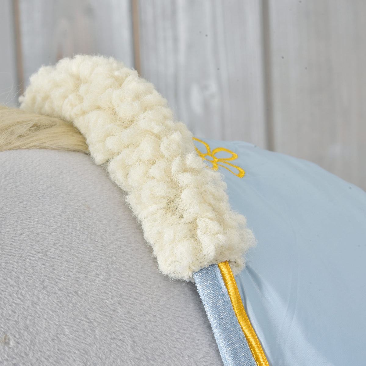 Gros plan sur le col en polaire bouclée crème, le passepoil jaune et la bordure pailletée bleue de la couverture d'écurie Misty sur un Hobby Horse gris