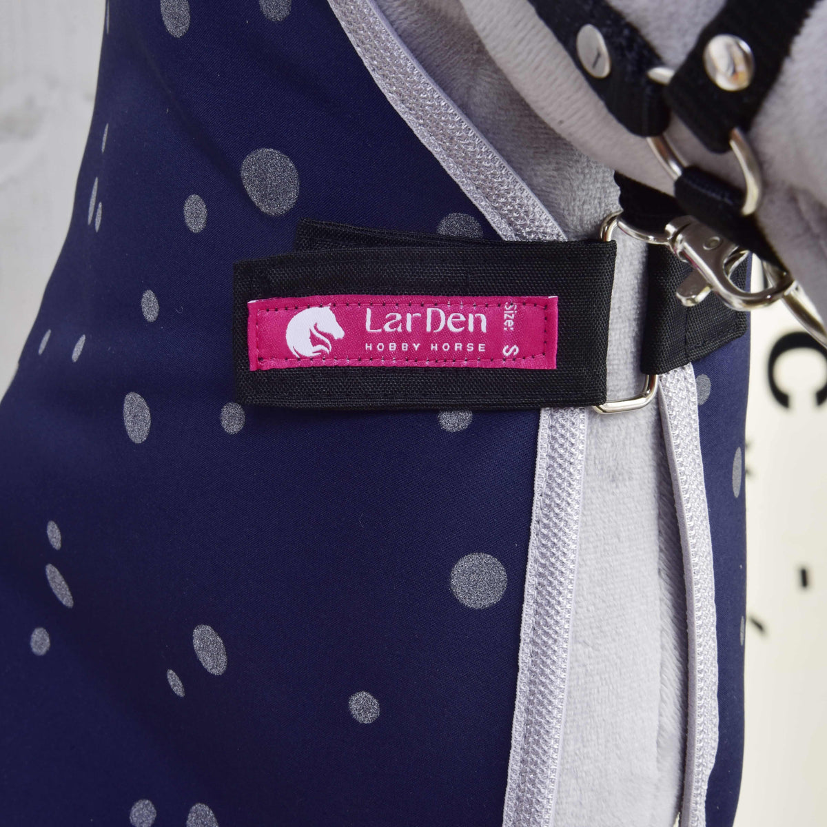 Close-up van het roze label met LarDen Hobby Horse op de zwarte borstriem van de marineblauwe gestippelde staldeken