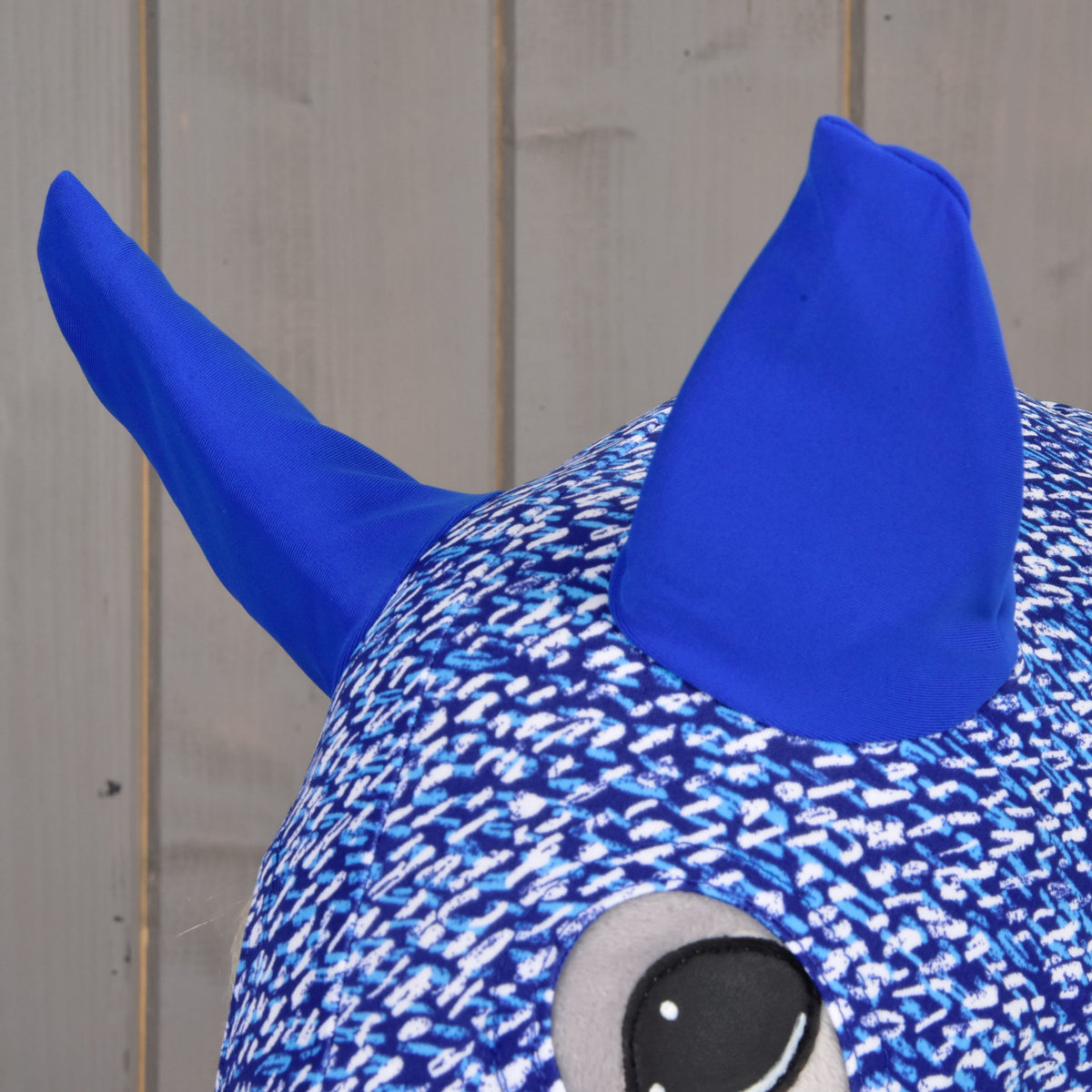 Close-up van de felle koningsblauwe oren en de oogopening van het bedrukte pak op een grijze Hobby Horse