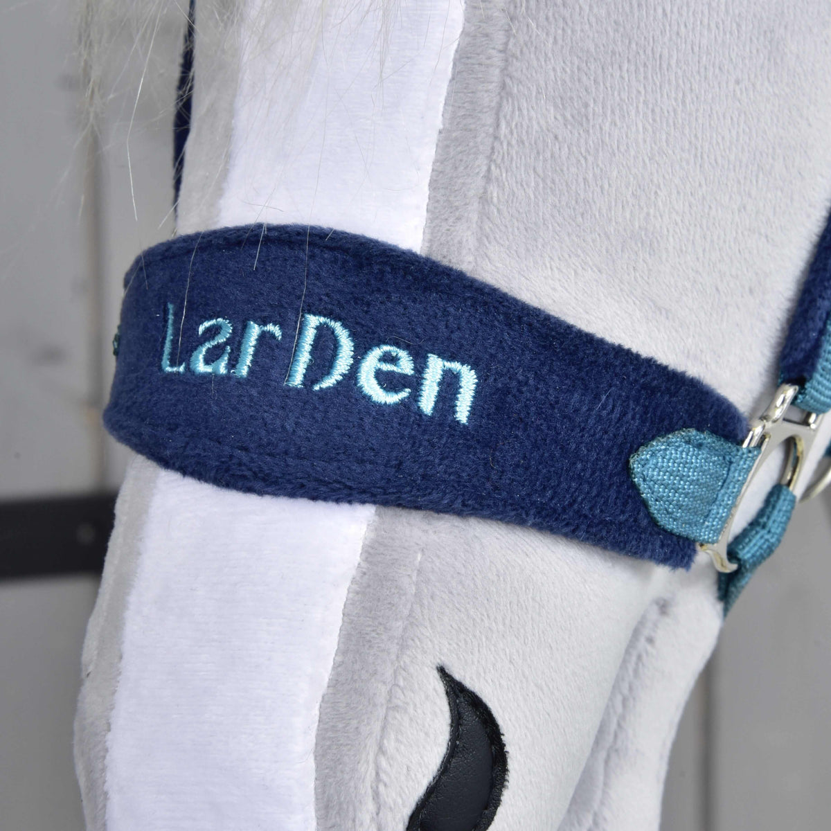 Close-up of the navy fleece noseband with LarDen embroidered in light blue, over the white blaze of a grey plush head