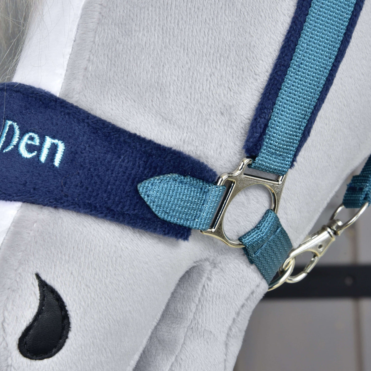 Close-up of the side ring where the teal cheek strap meets the navy fleece noseband, with the snap hook below