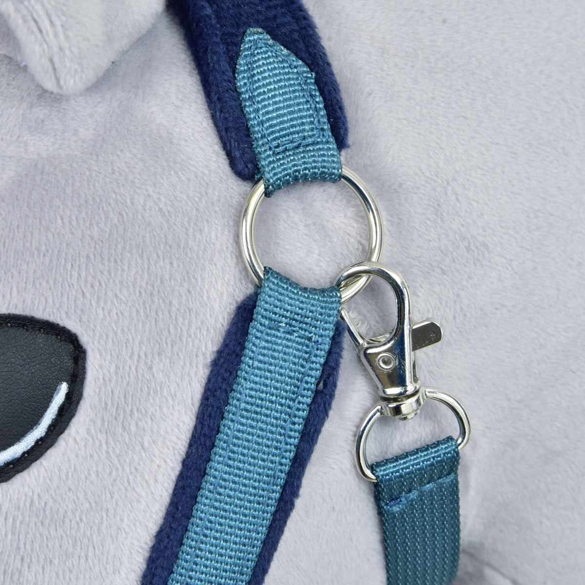 Close-up of the silver ring and snap hook on the teal throat strap of the blue fur halter, beside a stitched eye