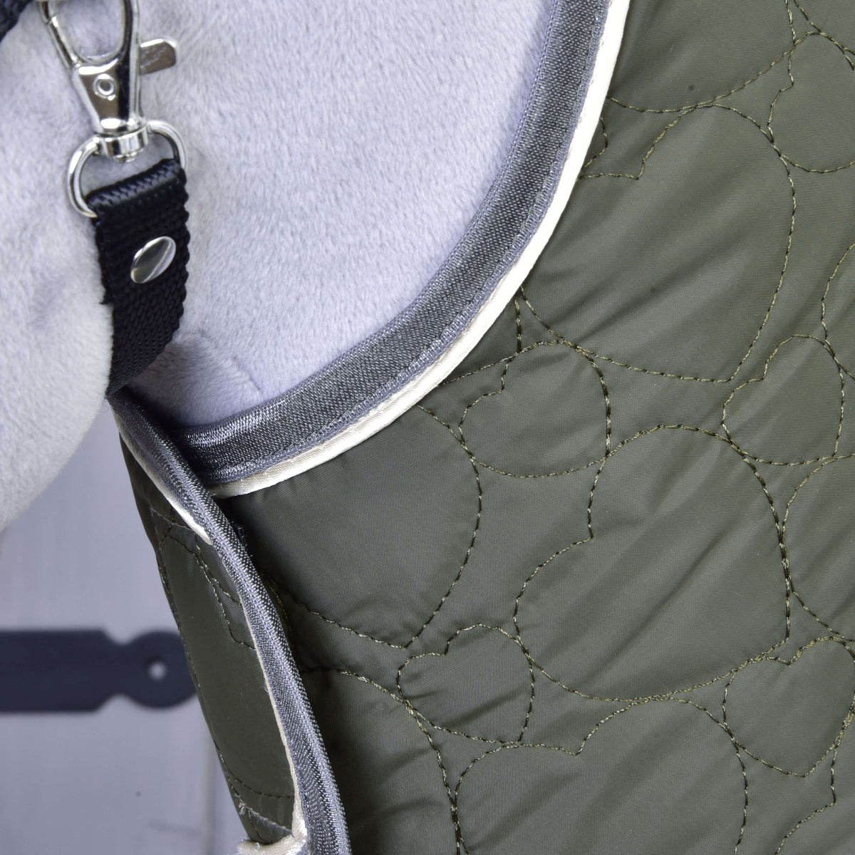 Gros plan sur les surpiqûres en cœurs et le passepoil gris et crème au cou de la couverture olive de l’ensemble Olivetti