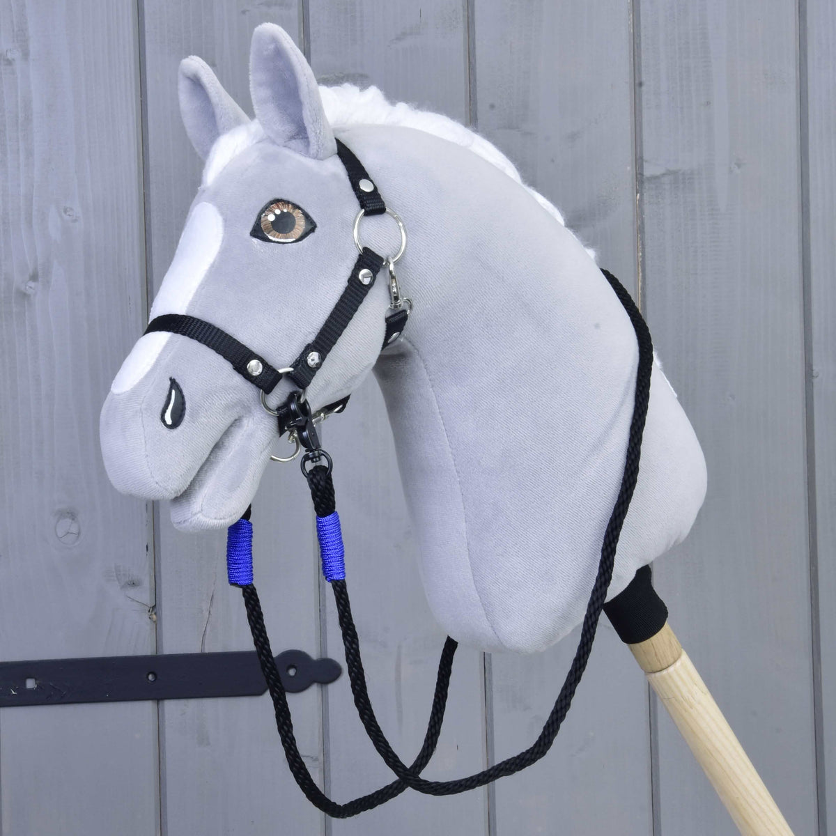 Grijze pluche Hobby Horse met zwart halster en de zwarte touwteugels met blauwe wikkels onder de kin vastgeklikt
