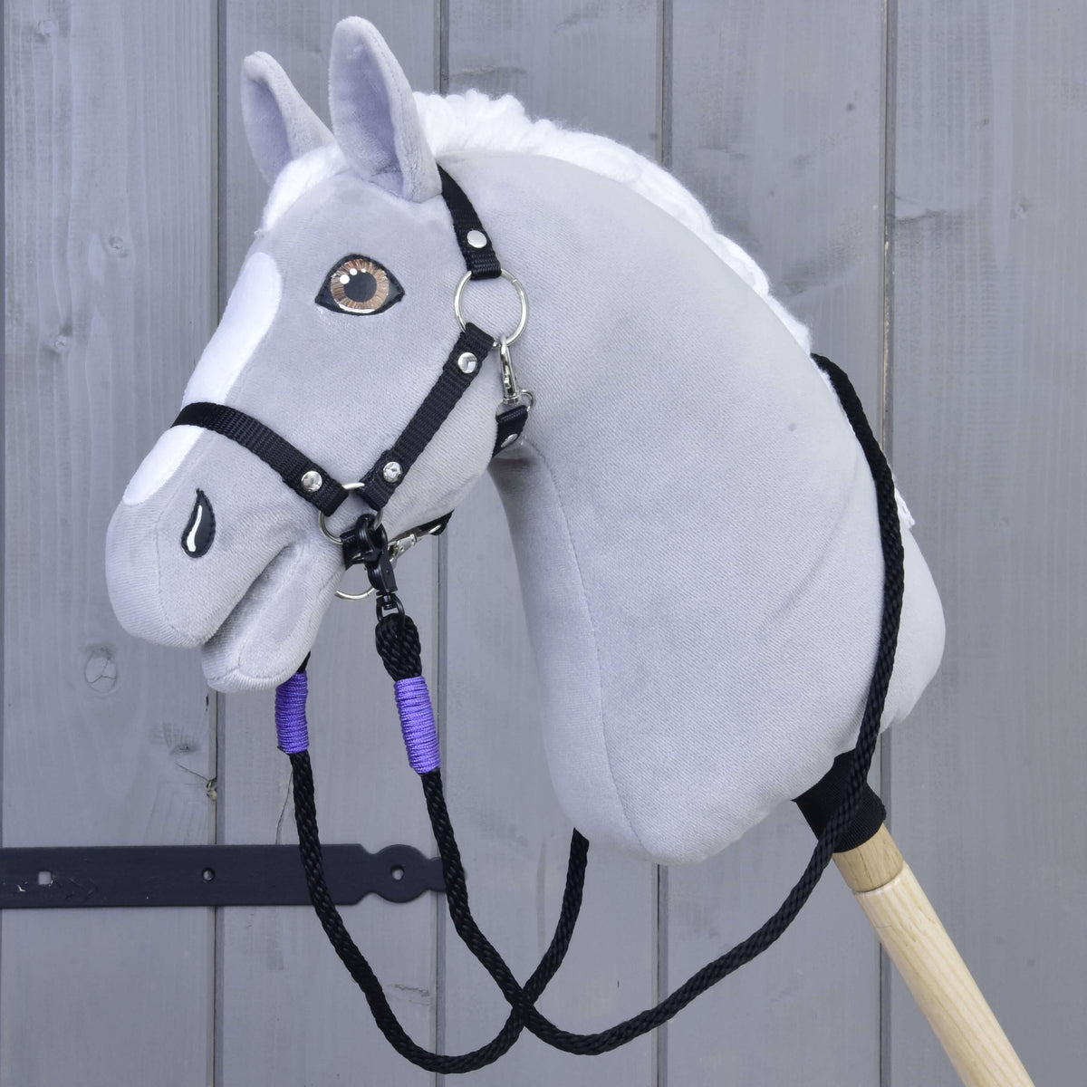 Grijze Hobby Horse met witte manen en zwart halster, de touwteugels met lila wikkels hangen in een lus eronder