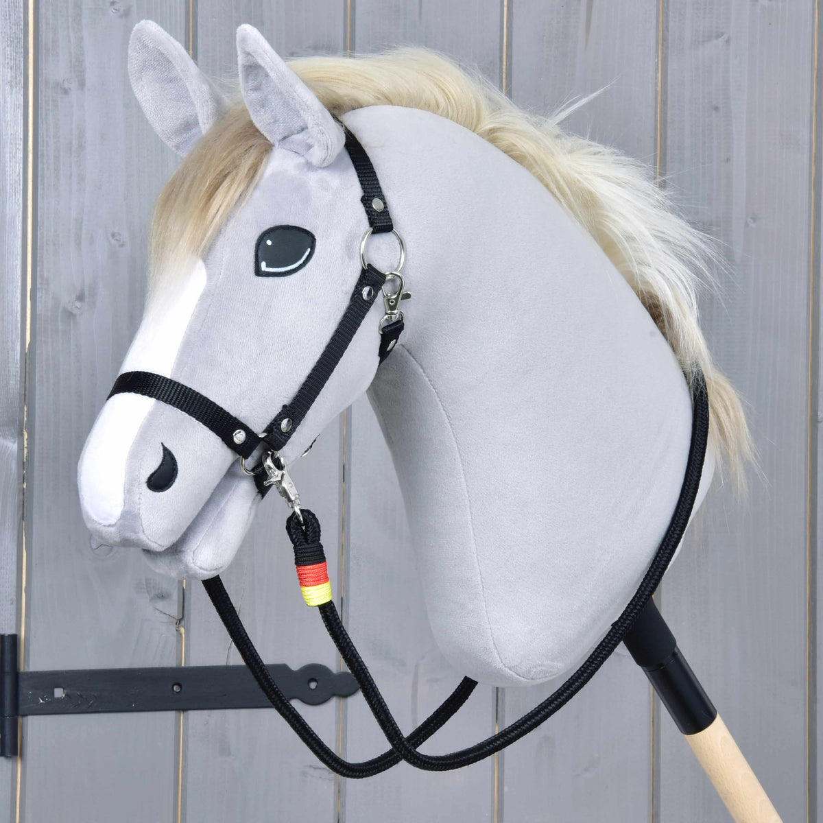 Grijze Hobby Horse met zwarte halster en de Teugels Emblem eraan vastgemaakt, de zwarte touwteugels hangen tot aan de stok