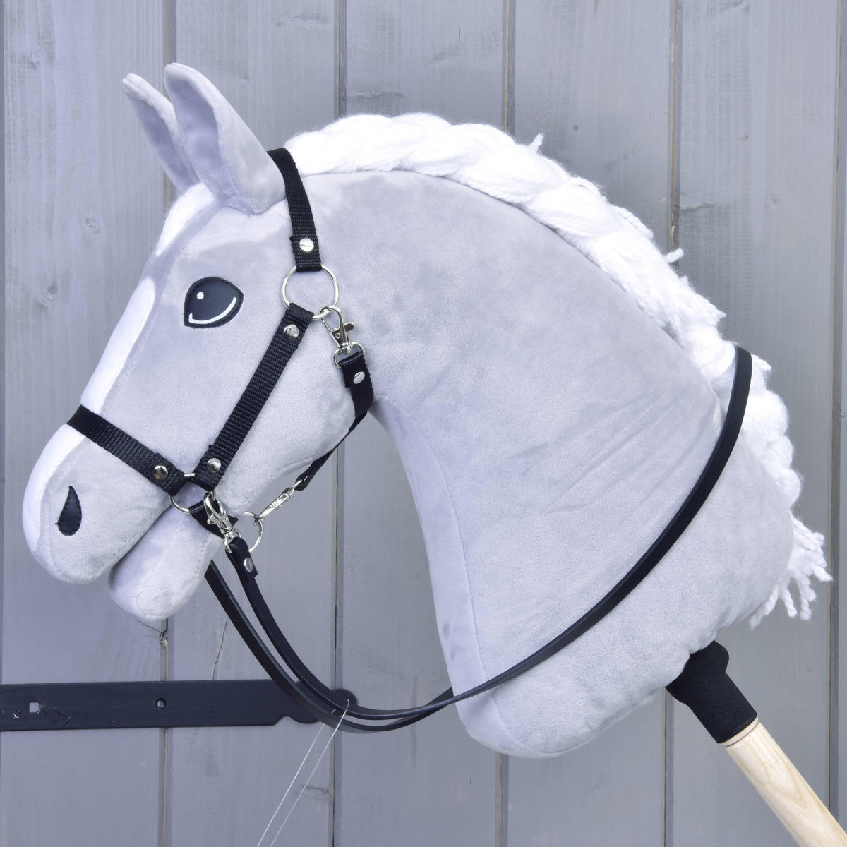 Zwarte teugels van kunstleer vastgeklikt aan het zwarte halster van een lichtgrijze Hobby Horse met gevlochten witte manen