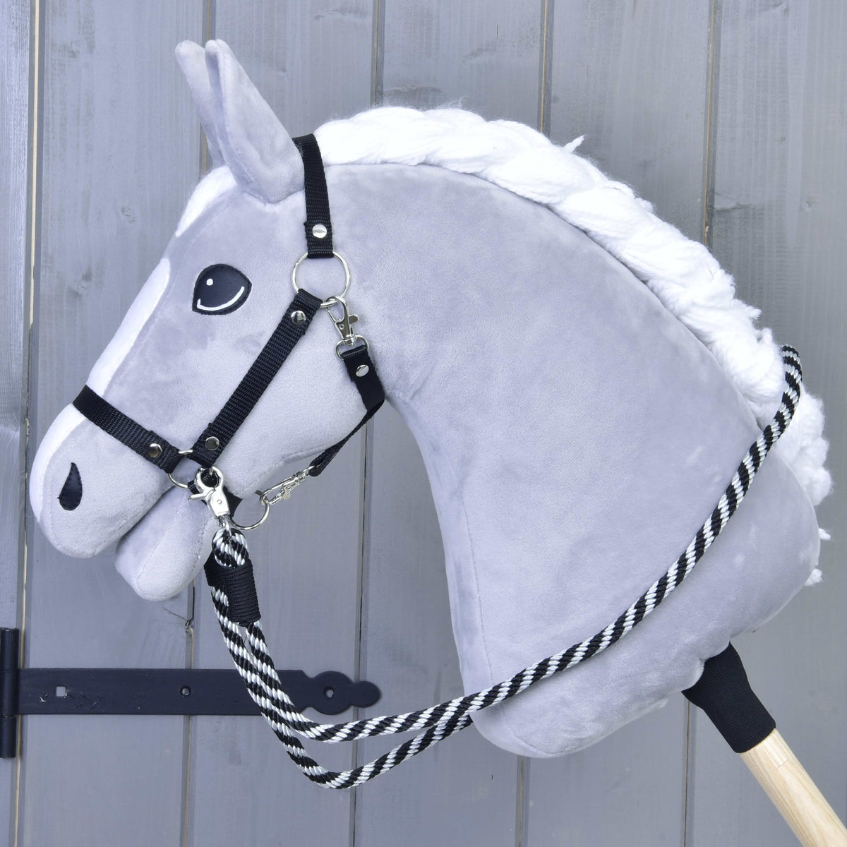 Hobby Horse gris à crinière blanche tressée avec licol noir, les rênes à rayures noires accrochées au licol