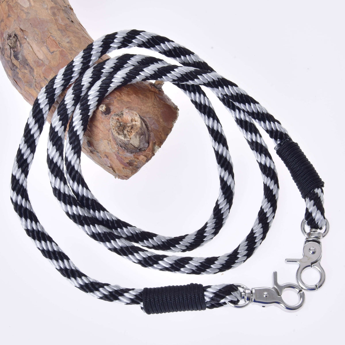Rênes à rayures noires pour Hobby Horse de LarDen, corde torsadée noire et blanche à deux mousquetons, posée sur une bûche