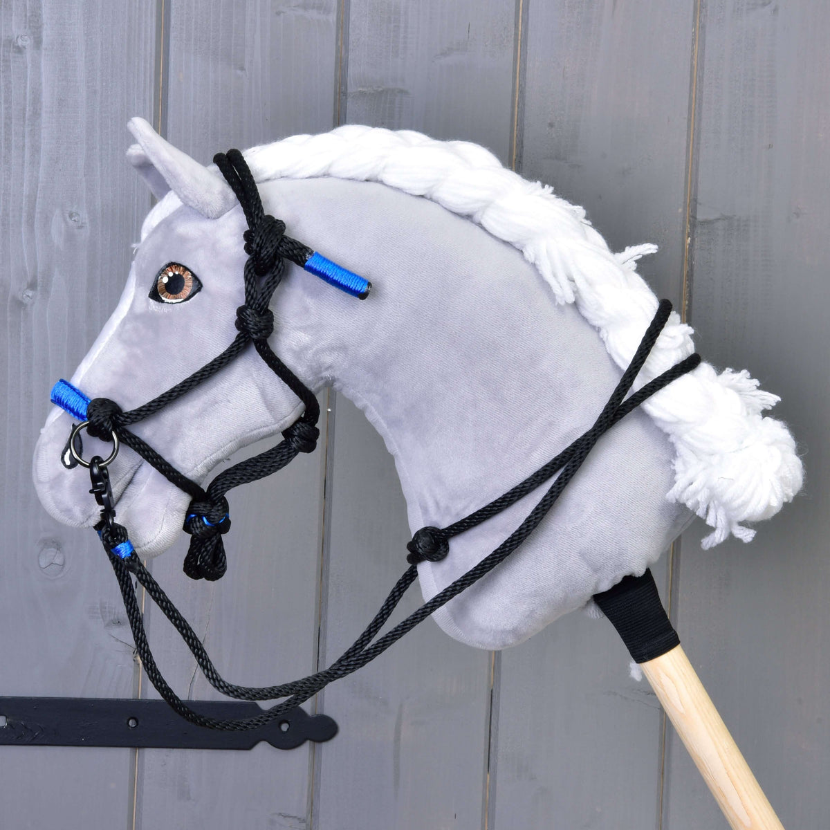 Een grijze pluche Hobby Horse met witte gevlochten manen draagt de zwart-blauwe touwhalster met zwarte touwteugels