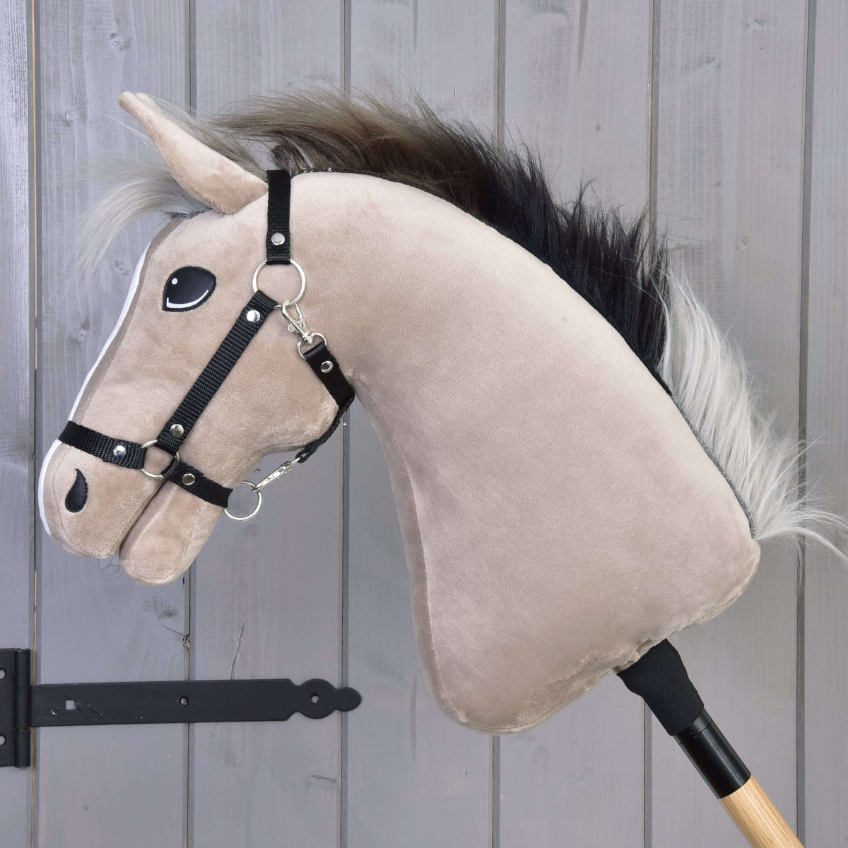 Hobby Horse Piccolino van links in profiel, met grijsbeige hals, zwarte halster en donkere manen met zilveren punten