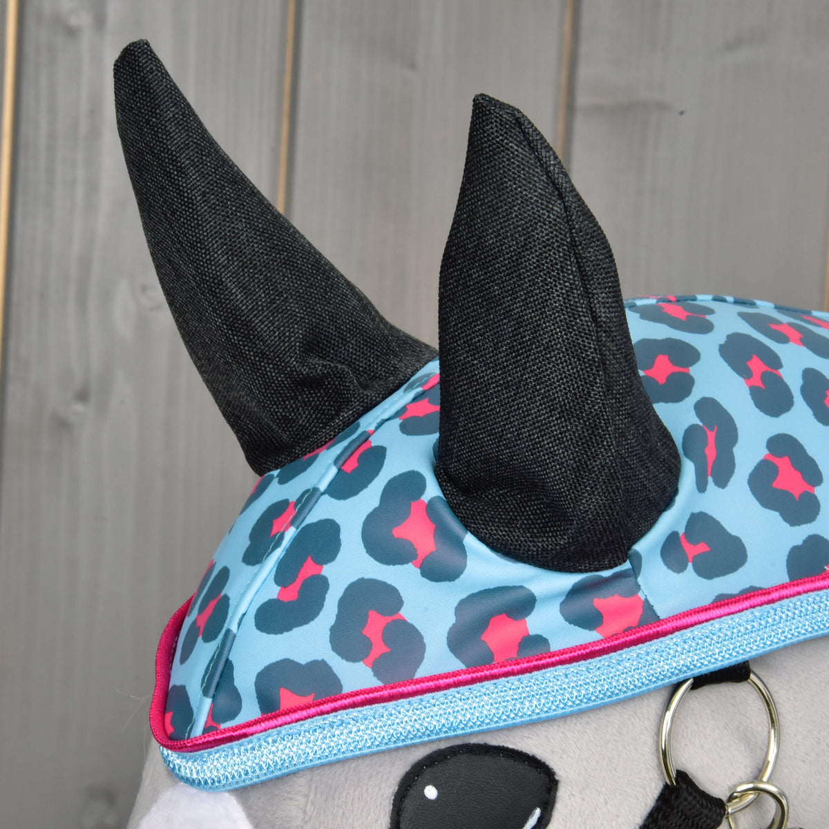 Close-up van de antracietkleurige oren op de capuchon met blauwe en roze luipaardvlekken en rand met roze bies