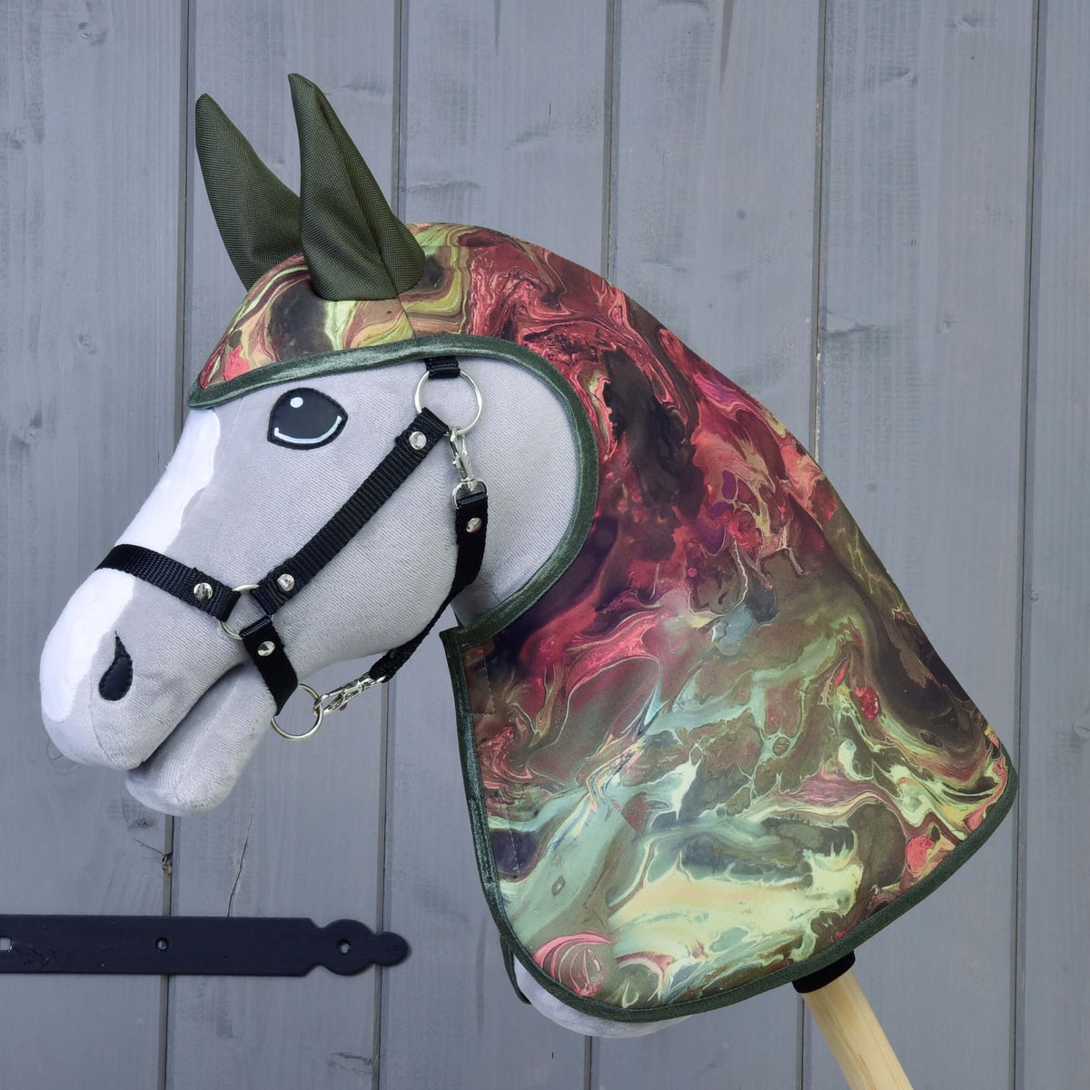 Een grijze pluche Hobby Horse met zwarte halster draagt de regenjas Galaxy met rood-groen marmerpatroon en olijfgroene oren