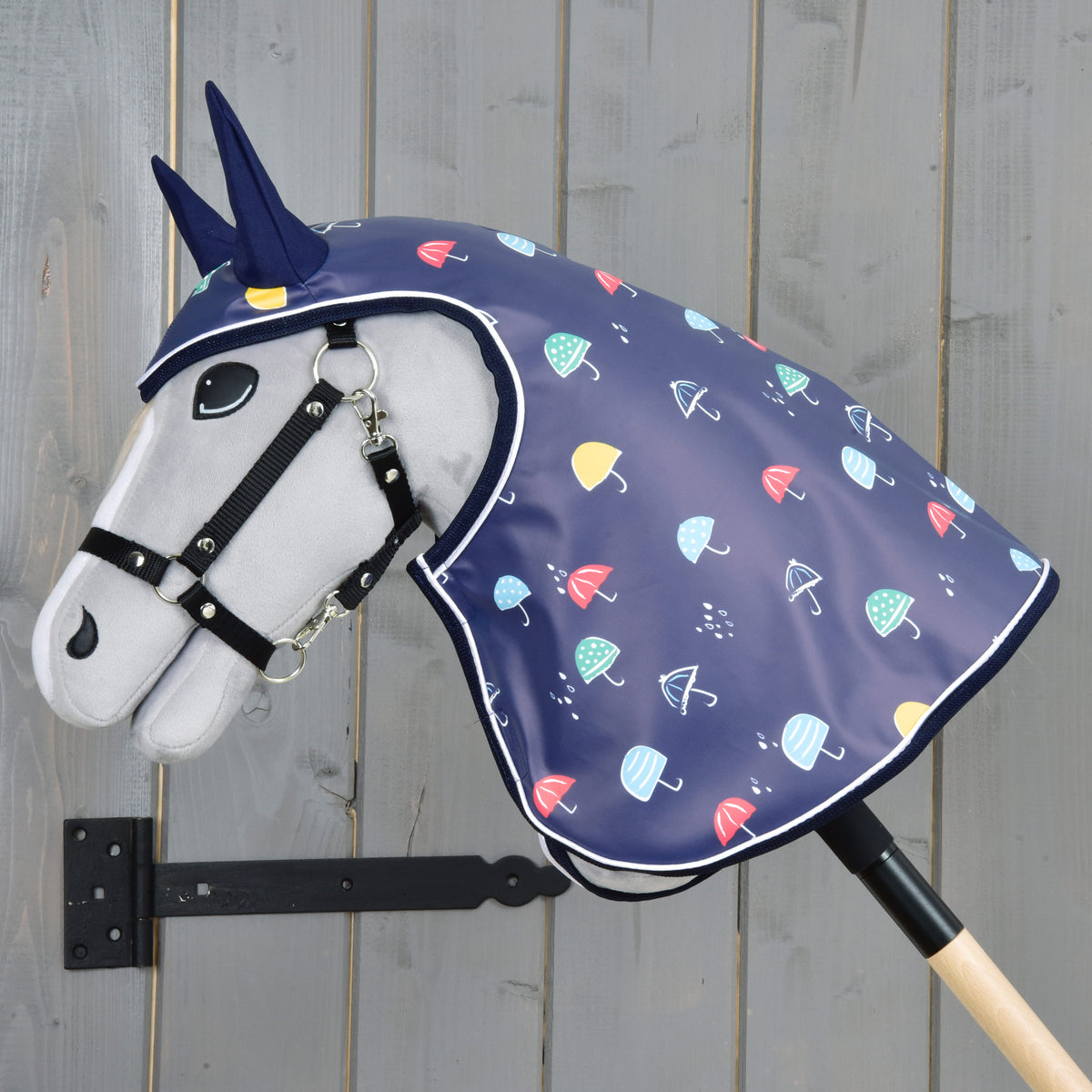 Hobby Horse gris vu de côté dans l’imperméable à parapluies, la capuche couvrant la tête et l’encolure jusqu’au bâton