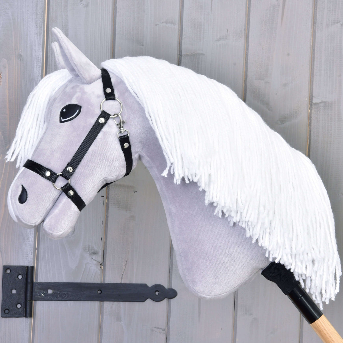 Side view of the light grey Hobby Horse with a long white yarn mane and black halter on a wooden stick