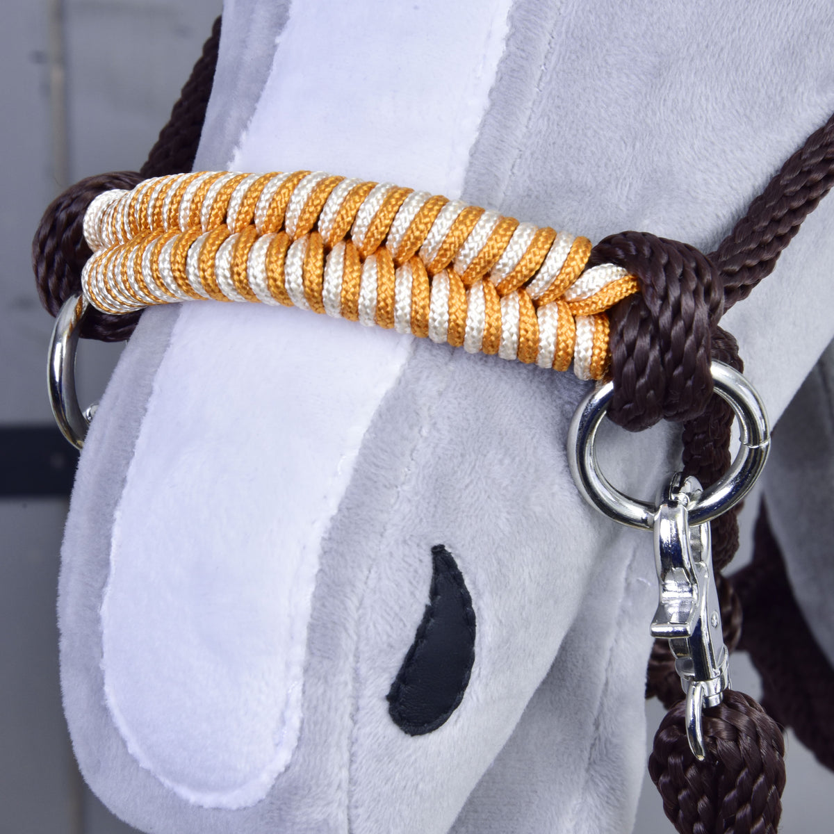 Detail van de oranje-wit gevlochten neusriem en de bruine knoop van de Hobby Horse Touwset Oranje op een grijs hoofd