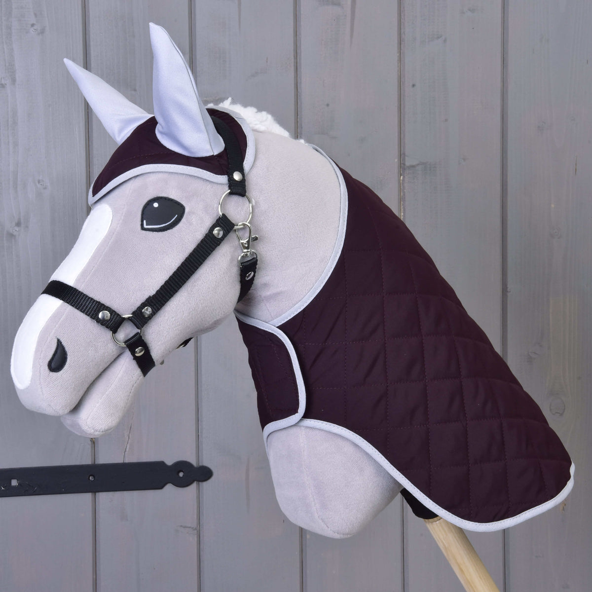 Light grey Hobby Horse in a black halter wearing the Set Purple: dark purple quilted ear bonnet and blanket
