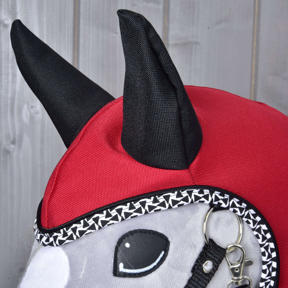 Close-up van de Regenjas Red Ferrari op een grijze Hobby Horse: zwarte stoffen oren op de rode kap en zwart-witte rand