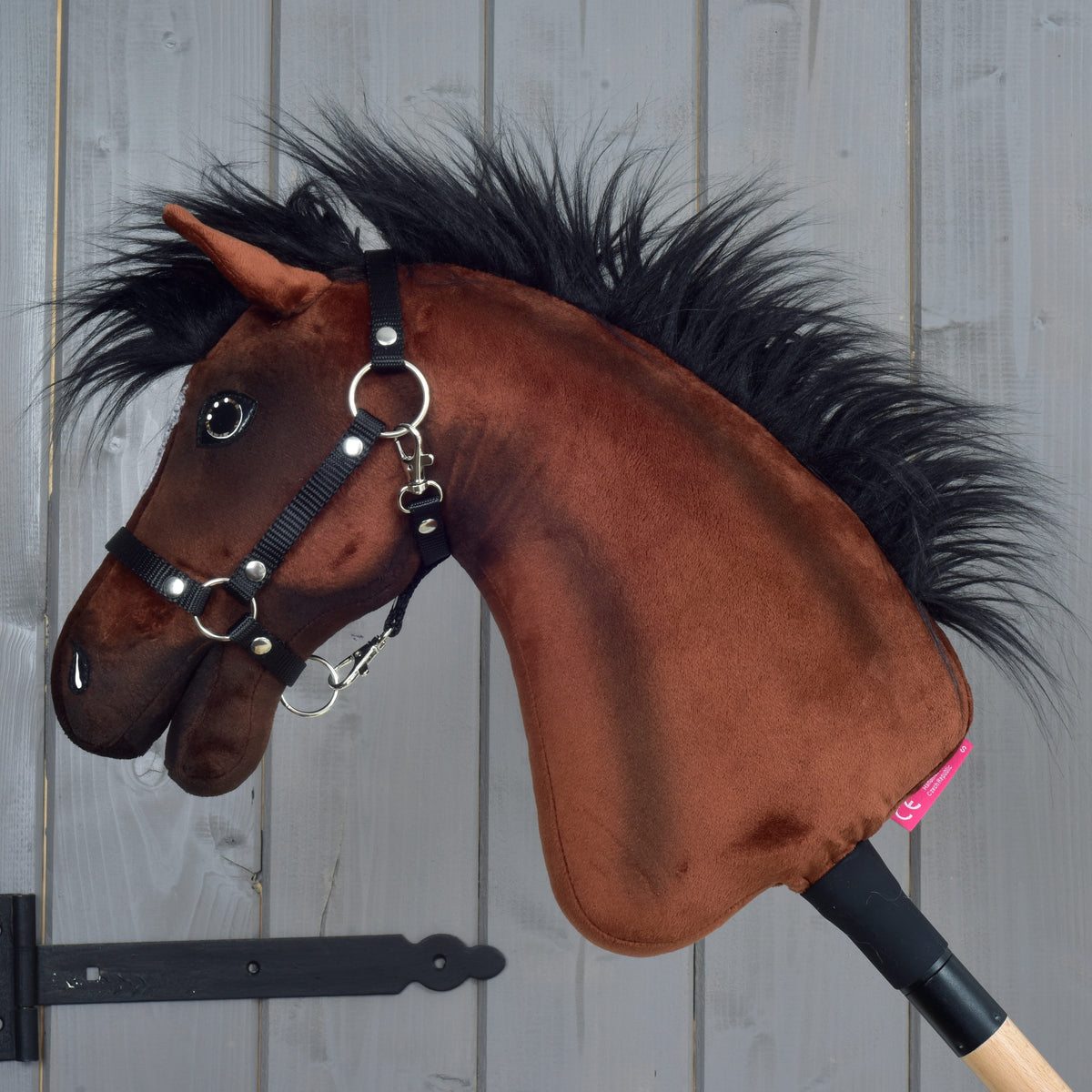 Hobby Horse Roger de profil gauche, peluche marron, longue crinière noire, licol noir en sangle et bâton en bois clair