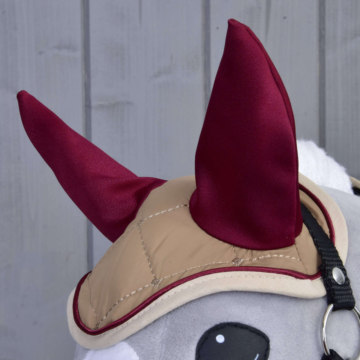 Gros plan sur le bonnet d’oreilles matelassé beige aux oreilles bordeaux, passepoil bordeaux et bordure crème sur un Hobby Horse