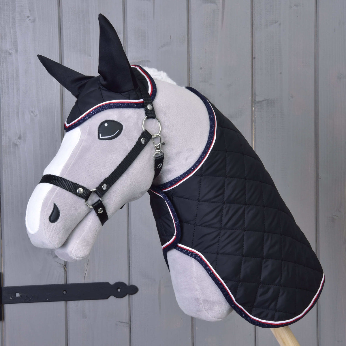 Hobby Horse gris en peluche à liste blanche et licol noir portant la couverture et le bonnet d’oreilles noirs matelassés de l’ensemble Royal