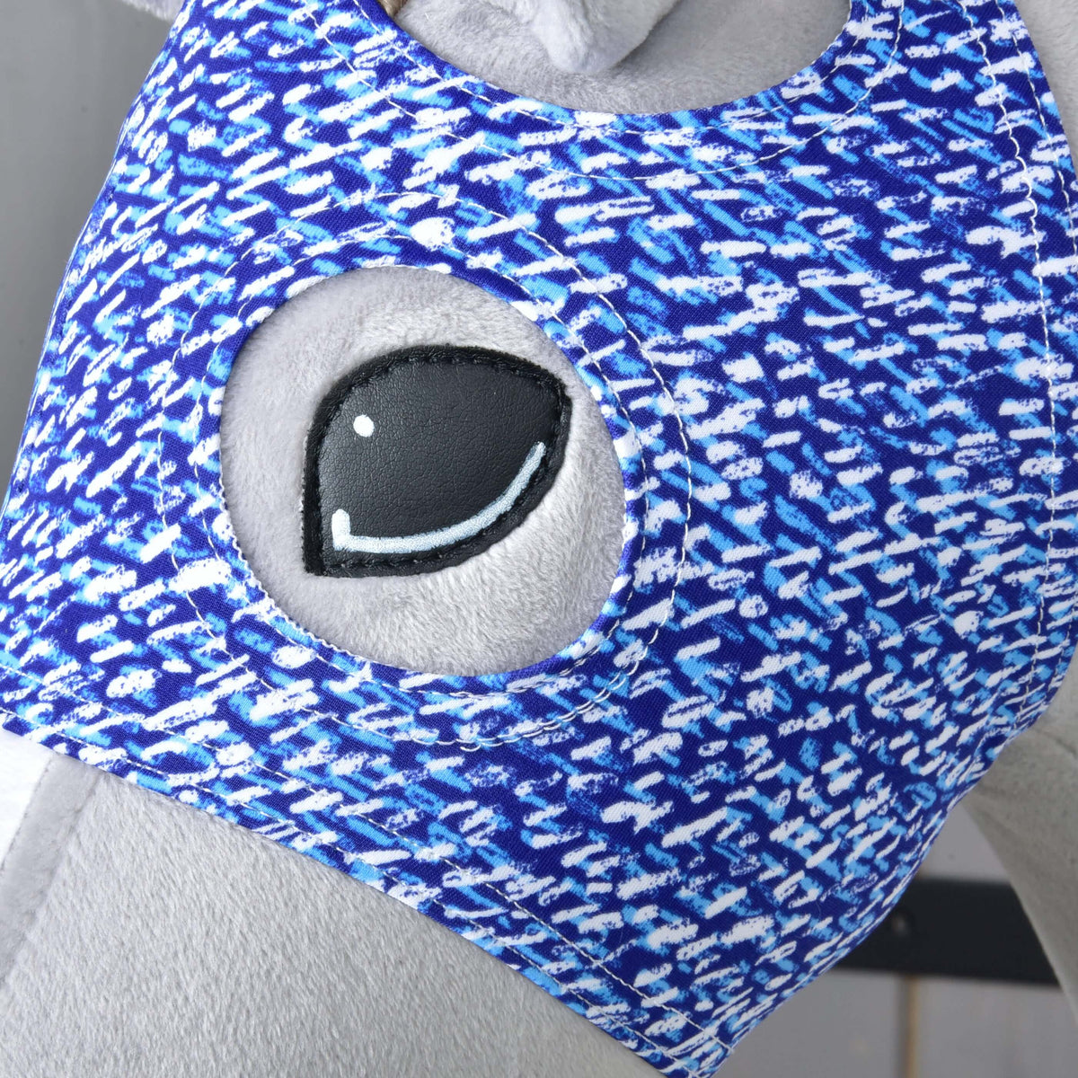 Close-up van de ronde oogopening van het blauwe masker rond het zwarte oog van een grijze Hobby Horse