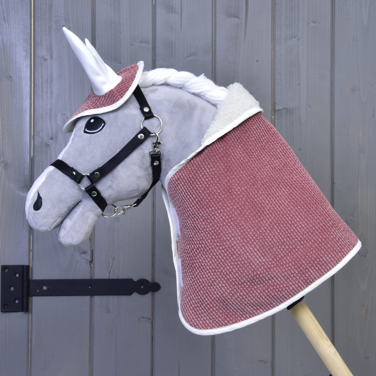 Grey plush Hobby Horse with a black halter wearing the Set Manchester Tea Rose blanket and ear bonnet in dusty pink